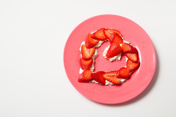 heart shaped strawberry in a pink plate on white background