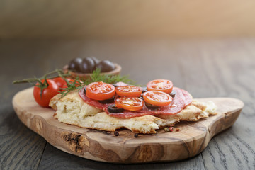 flat pita bread with salami and vegetables on wood table