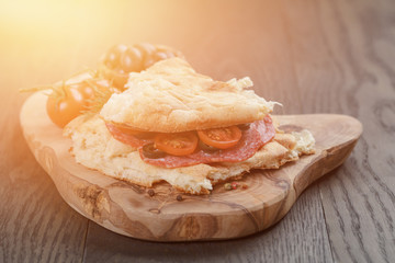 flat pita bread with salami and vegetables on wood table