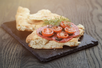 flat pita bread with salami and vegetables on slate board