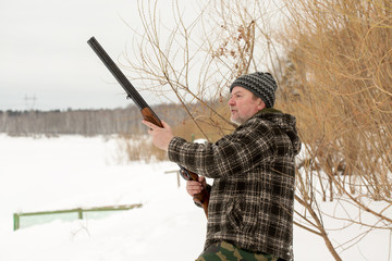 A hunter shooting a rifle in winter snowy landscape