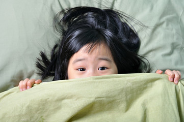 Scared little asian girl hiding behind blanket