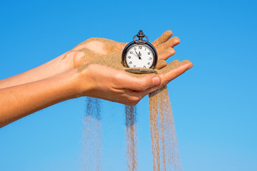 pocket clock in hands and sand flowing