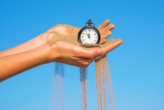 pocket clock in hands and sand flowing - Powered by Adobe