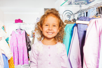 Cute girl among clothes on the hanger in  shop