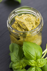 Glass jar with basil pesto on a black plate