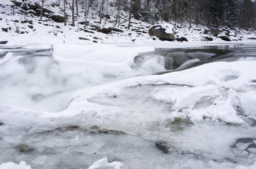 Fototapeta na wymiar Ice covers rocks in a slow motion river in the winter