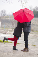 Couple kissing behind a red umbrela