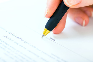 Woman at office desk signing a contract with shallow focus on si