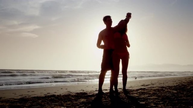 couple doing pirouette on beach - silhouette of man and woman dancing in front of sun on sand - slow motion 4K
