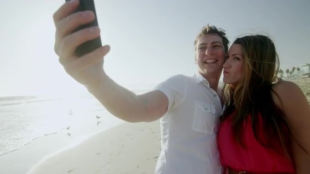 attractive couple taking selfie on beach by ocean - gorgeous man and woman taking picture on vacation in 4K and 1080 HD