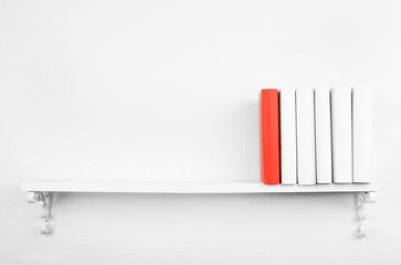 Blank books with red one on bookshelf on white wall background