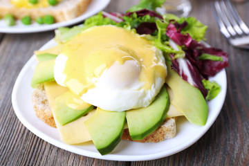 Toast with egg Benedict and avocado on plate on wooden table