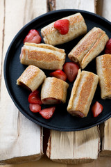 Frying pan with strawberry stuffed pancakes on wooden logs