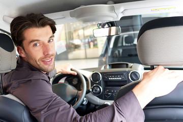 smarter junger Mann testet Auto im Autohaus
