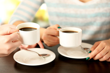 Two women with cups of coffee on bright background
