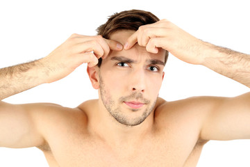 Handsome young man squeezing pimple isolated on white