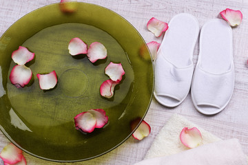 Spa bowl with water, rose petals, towel and slippers