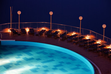 Sun loungers on the poolside in a night scene.