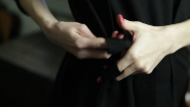 woman tying belt of black dress, finishing clothes