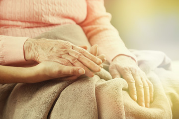 Old and young holding hands on light background, closeup