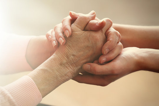 Old and young holding hands on light background, closeup