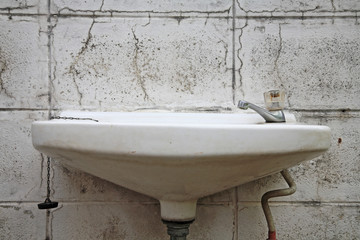 Old white washbasin on dirty wall