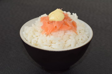 Sushi with salmon and sauce in a bowl on a black background.