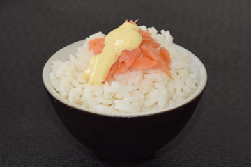 Sushi with salmon and sauce in a bowl on a black background.