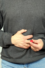 Mann mit Bauchschmerzen hält rote Tablette