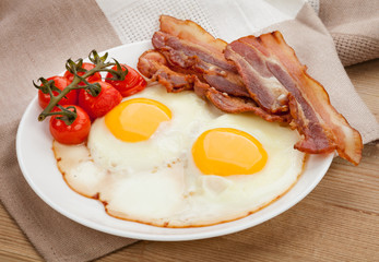 Plate with fried eggs, bacon on board