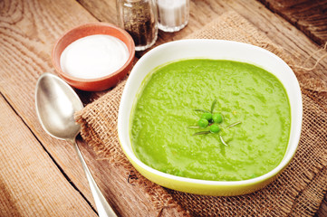Green pea soup in a bowl with bread and sour cream on line table
