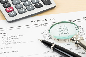 Balance sheet financial report with magnifier, pen, and calculat