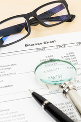 Balance sheet financial report with pen, magnifier, and glasses