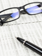 Pen and glasses rest on stock price detail financial newspaper