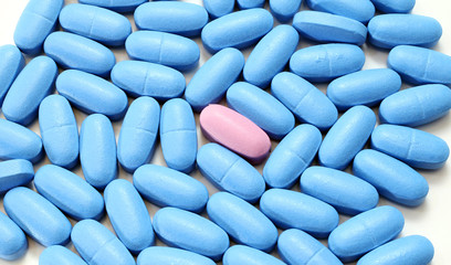 large pink pill among many blue pads