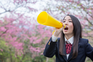 桜をバックにメガホンで応援をする女子学生