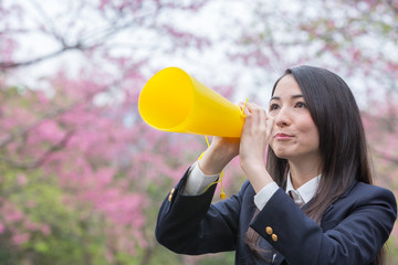 桜をバックにメガホンで応援をする女子学生