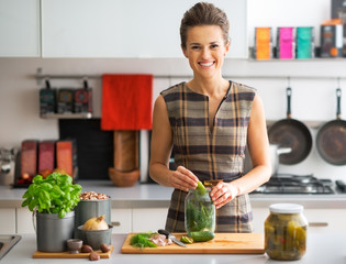 Portrait of happy young housewife pickling cucumbers in kitchen