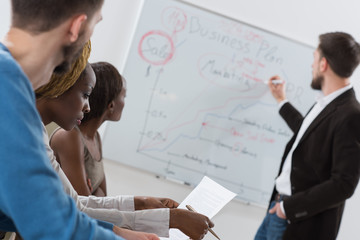 Handsome man presenting charts on whiteboard to team - obrazy, fototapety, plakaty