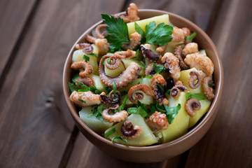 Octopus salad with boiled potato and parsley over wooden surface