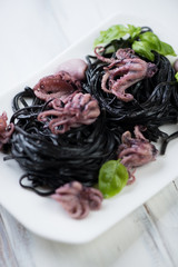 Close-up of squid ink tagliatelle with baby octopuses and basil