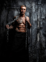 Muscular strong male with tattoo poses holding steel chain