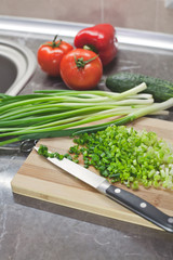 Chopped green onions and vegetables on striped wooden board