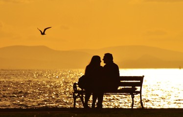 Fototapeta na wymiar Young couple sitting on a bench under sunset