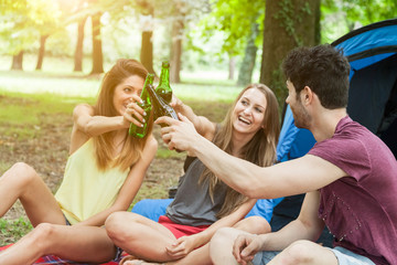 Fototapeta premium Three friends in camp celebrating by drinking a beer