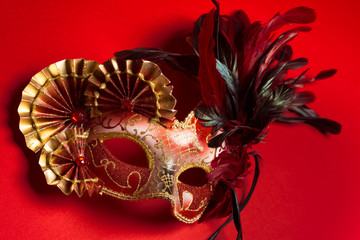 A red and gold feathered Venetian mask on red background