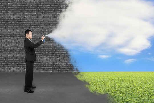 Businessman spraying clouds sky grass paint cover old brick wall