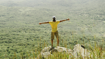 Fototapeta na wymiar Man standing with raised arms on peak of rock in summer