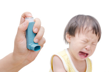 Woman's hand holding asthma inhaler foreground and crying baby s